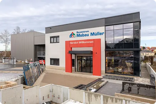 Bauzentrum Mobau Müller in moderner Architektur mit einladendem Eingangsbereich und großflächigen Fenstern, umgeben von Baumaterialien und dem Baustellenbereich.