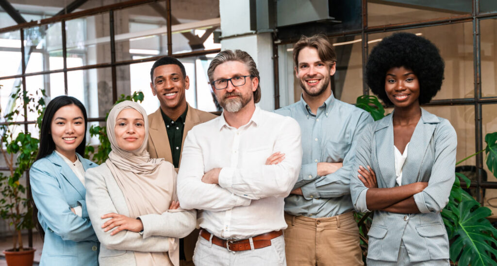 Sechs diverse Fachleute stehen aufrecht in einem modernen Büro, lächelnd und selbstbewusst.