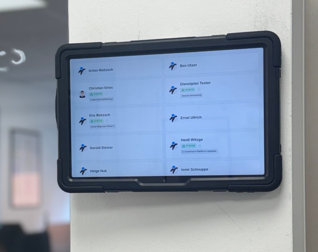 Digitale Anzeige im Büro mit Namen und Aufgaben von Mitarbeitenden, darunter Anton Roitzsch, Christian Gries, Eric Roitzsch und weitere. Die Anzeige zeigt aktuelle Projekte und Zeitangaben.
